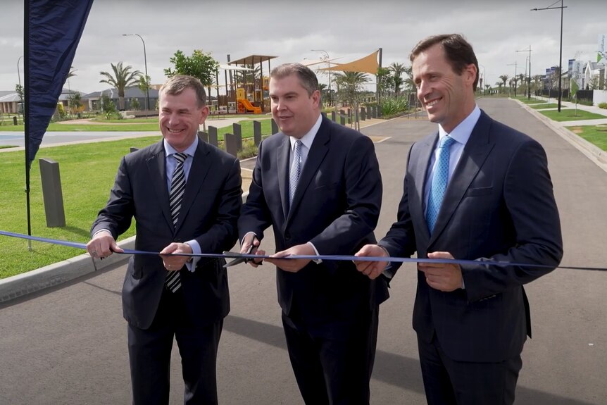 Three men cut a ribbon.