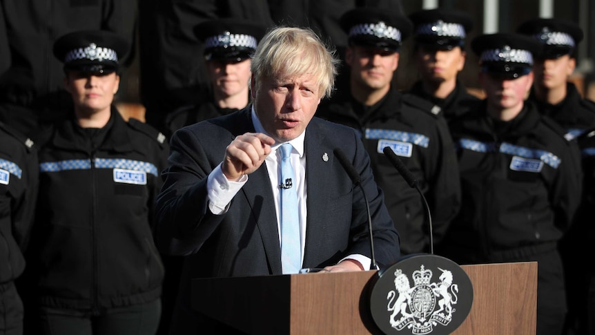 Boris Johnson gives a speech at a podium in front of police officers.