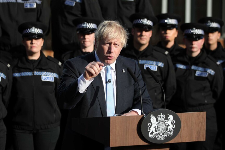 Boris Johnson gives a speech at a podium in front of police officers.