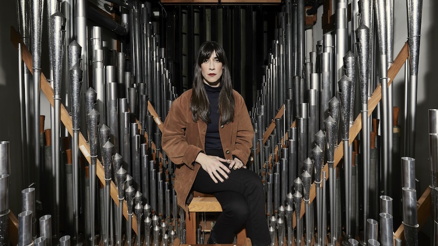 A woman sits among many silver pipes inside the Melbourne Town Hall grand organ.