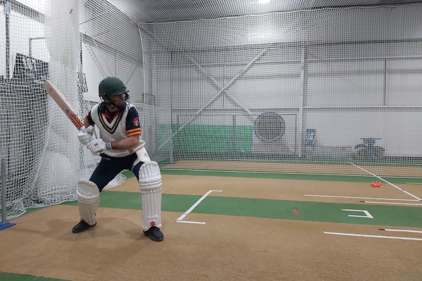 a man wearing cricket pads on his legs leans in to hit a ball in practicing nets