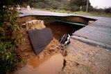 A large sink hole in the road with a car in it