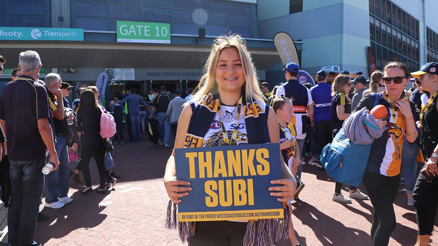 Annelise Hill, dressed in West Coast Eagle stiped scarf and AFL jersey, holds a sign saying "Thanks Subi".