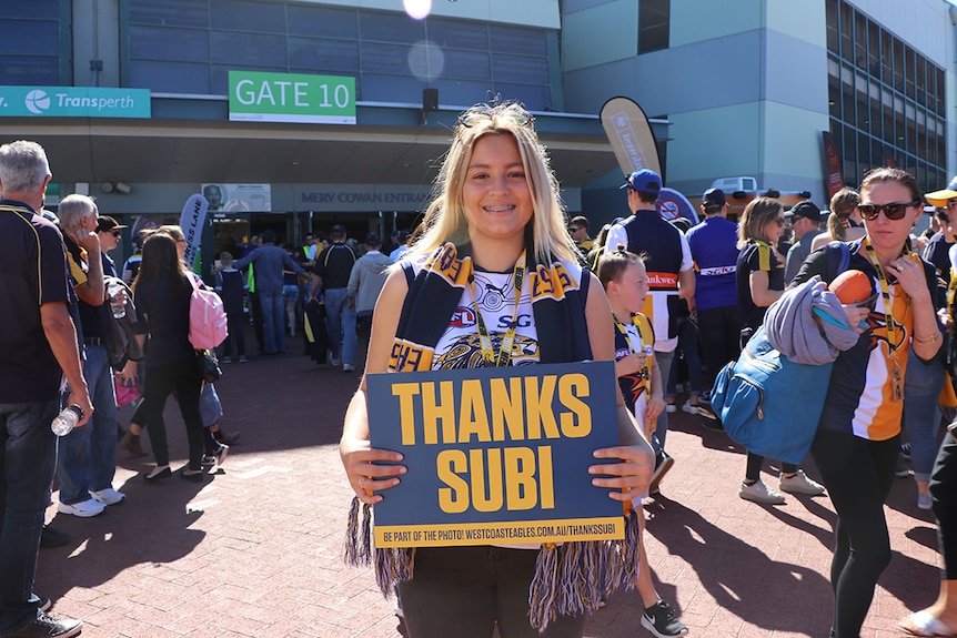 Annelise Hill, dressed in West Coast Eagle stiped scarf and AFL jersey, holds a sign saying "Thanks Subi".