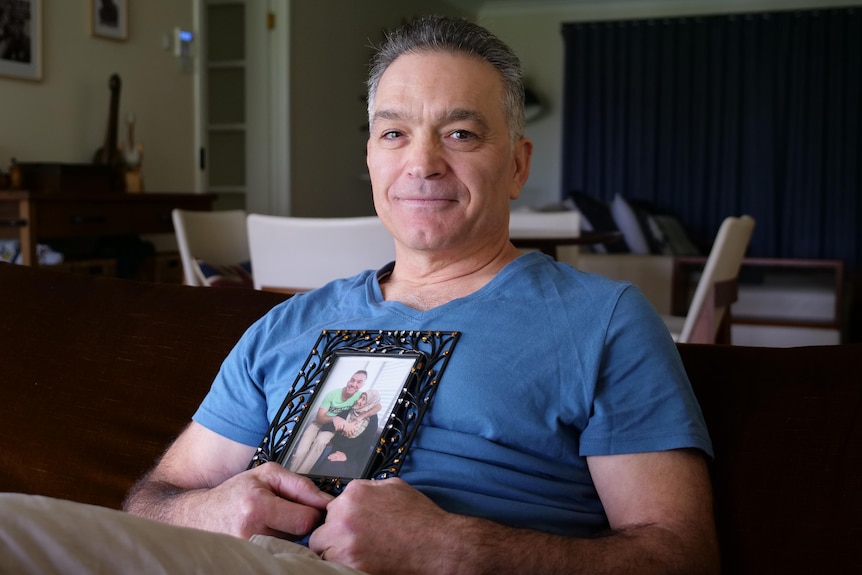 A man in a blue t-shirt holding a photo of himself and a woman wearing a hair covering