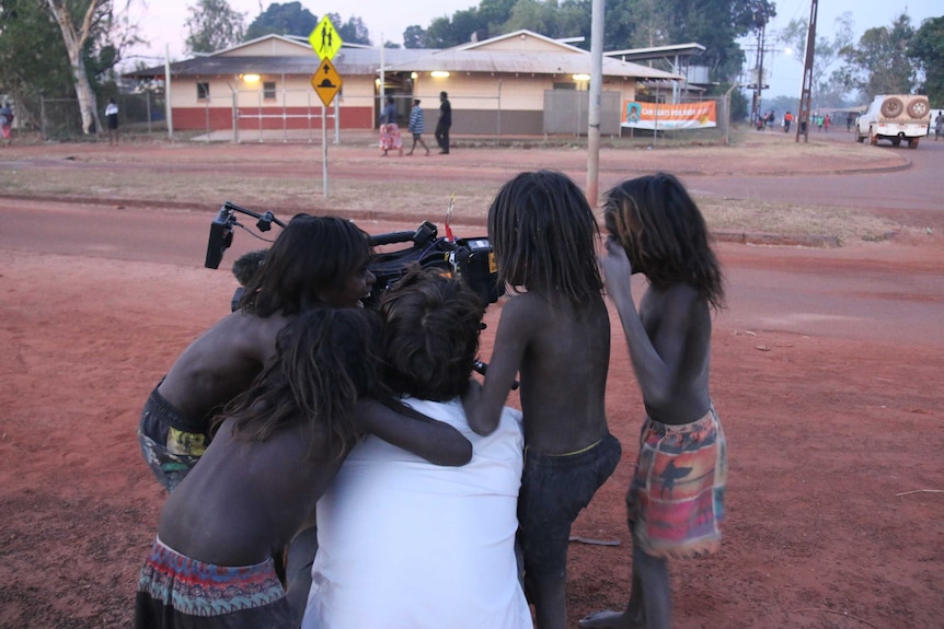 Indigenous children in Wadeye crowd around cameraman Hamish Harty to look at the playback screen.