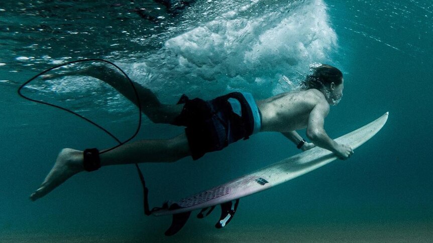 A surfer dives under a wave with his board.