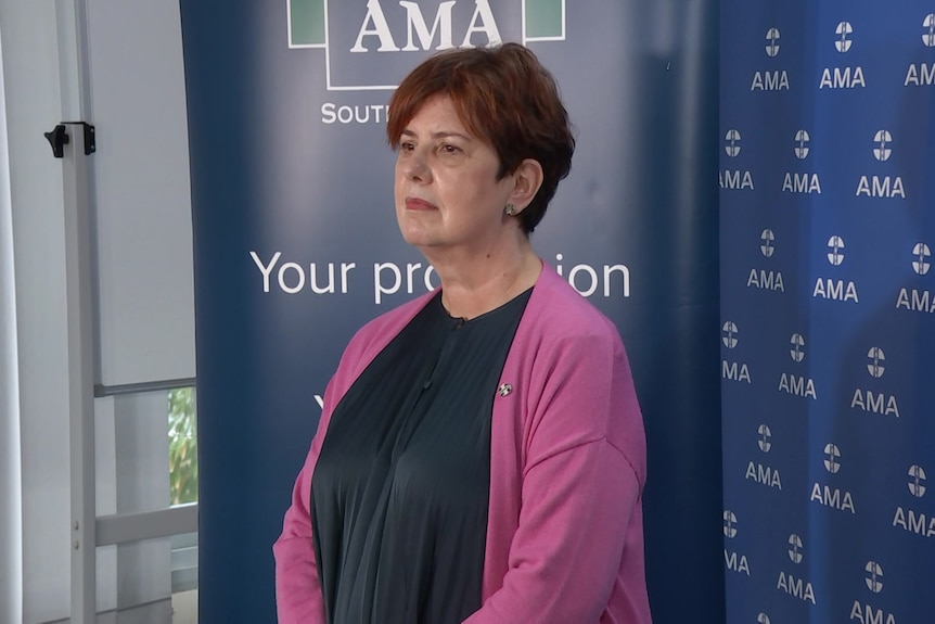 A woman wearing a pink cardigan standing in front of a blue banner saying AMA on it