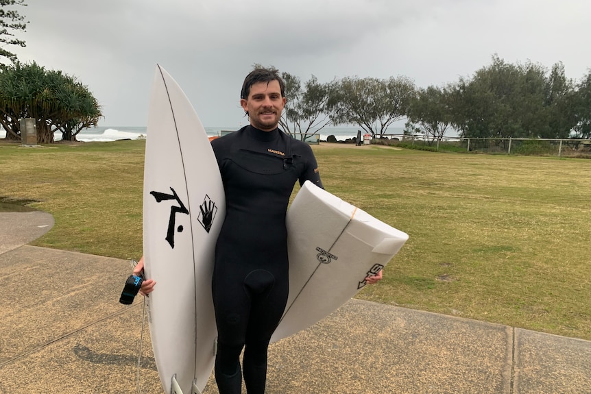 A surfer on the beach in a wetsuit with one broken board and another board.