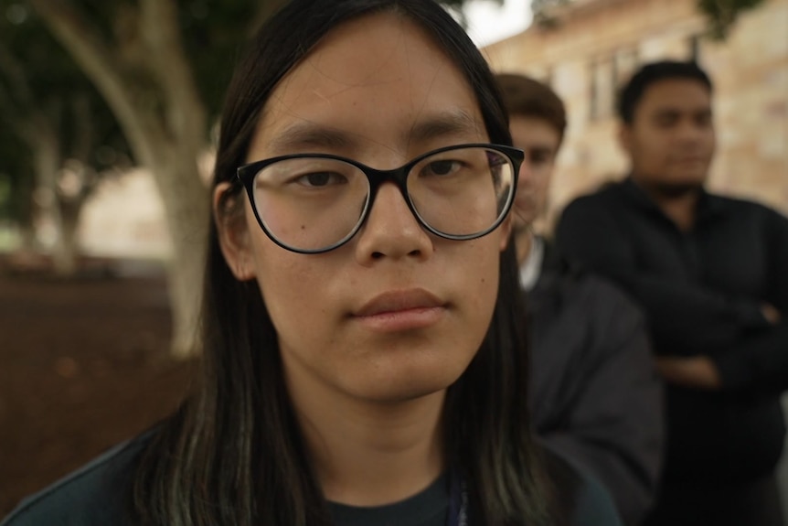 A woman with glasses looks at the camera.