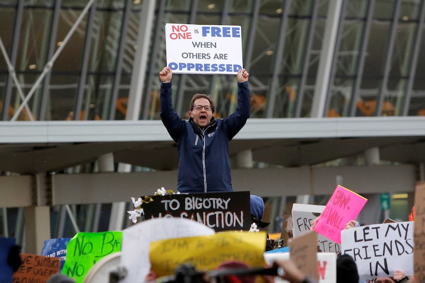 A man yells and holds a sign saying "No one is free when others are oppressed"
