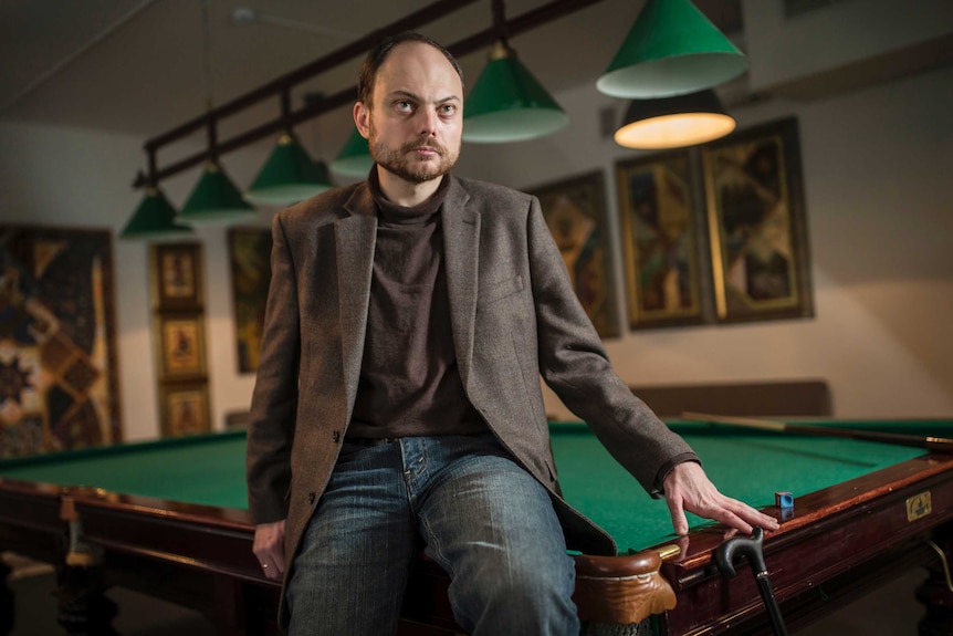 Russian opposition activist Vladimir Kara-Murza sits on a pool table dressed in trousers and a suit jacket.