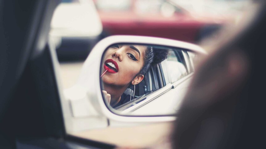 Woman applying lipstick in the side mirror of her car for a story about how a woman's appearance affects her career