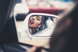 Woman applying lipstick in the side mirror of her car for a story about how a woman's appearance affects her career
