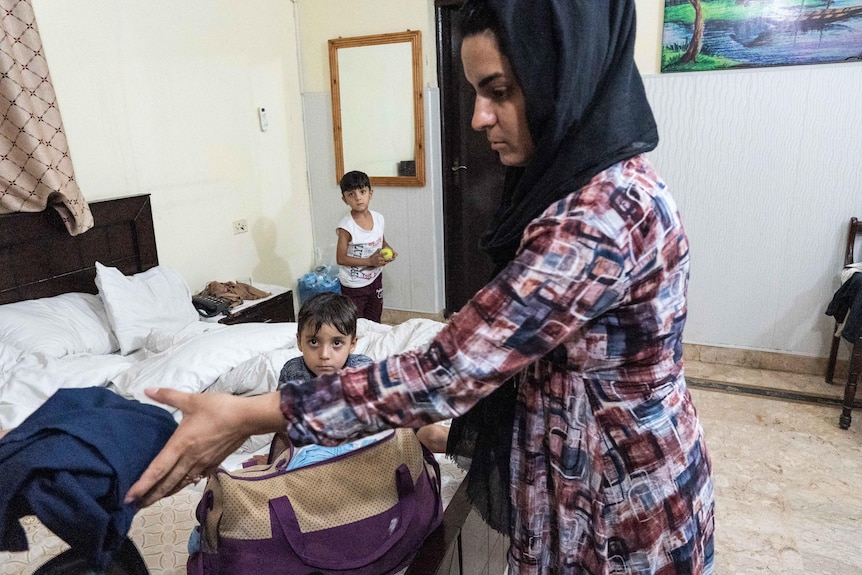 A woman holds out her hand ofr a piece of clothing as two children look on.