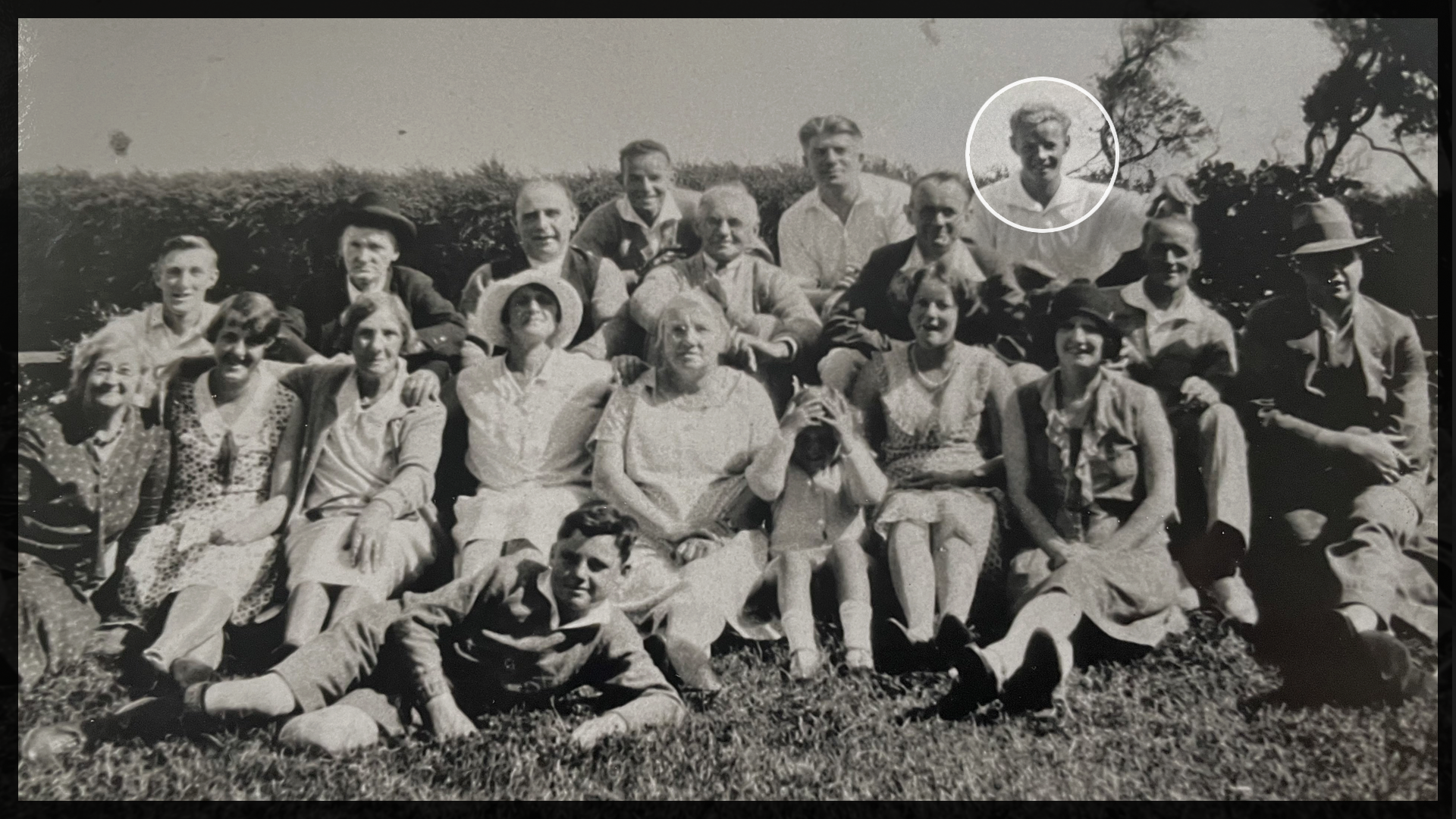 Black and white large family group photo from early 1900s. A man is circled patting his hand on another man's head as a joke