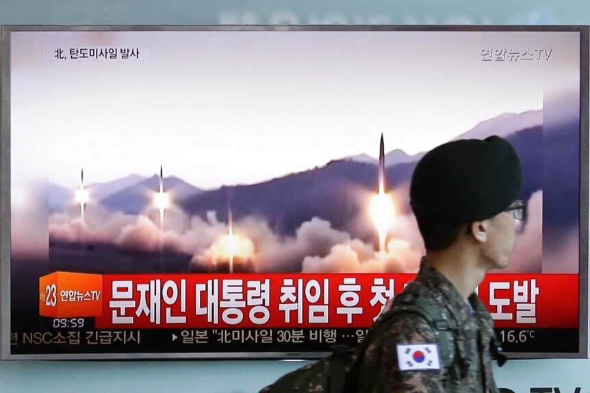 A South Korean army soldier walks by a TV news program showing a file image of missiles being test-launched by North Korea.