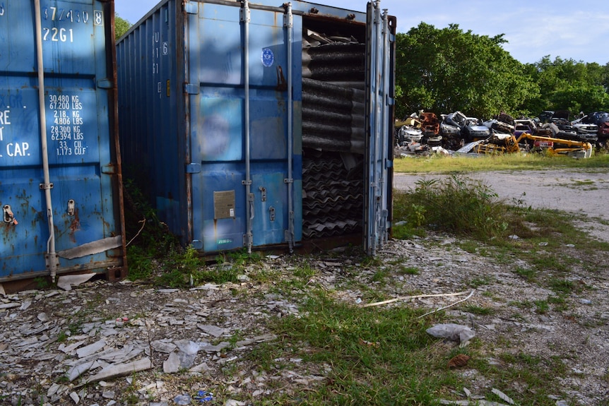 A blue shipping container's door is open, and sheets of asbestos are packed to the top.