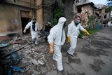 Emergency management specialists in protective clothing transport the covered body of a person out of a bombed building. 