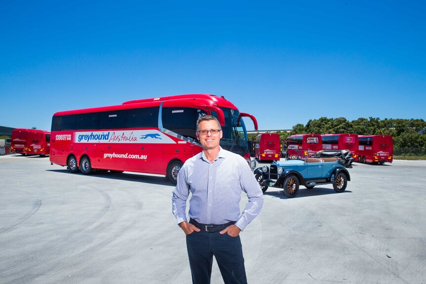 A man standing in front of a red coach with his hands in his pocket.