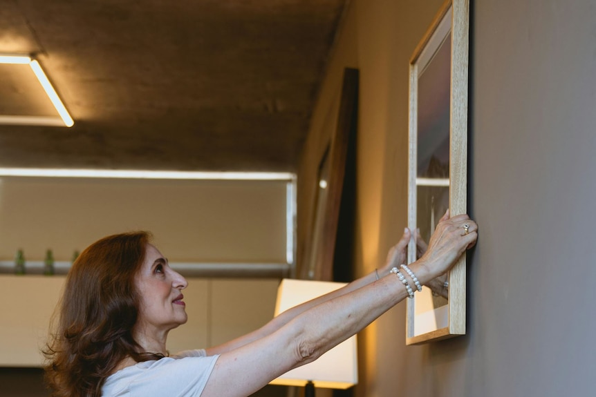 A woman leans forward to hang a picture.