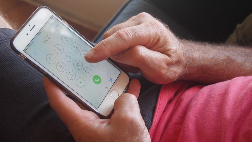Closeup of man's hand dialling 000 on iphone