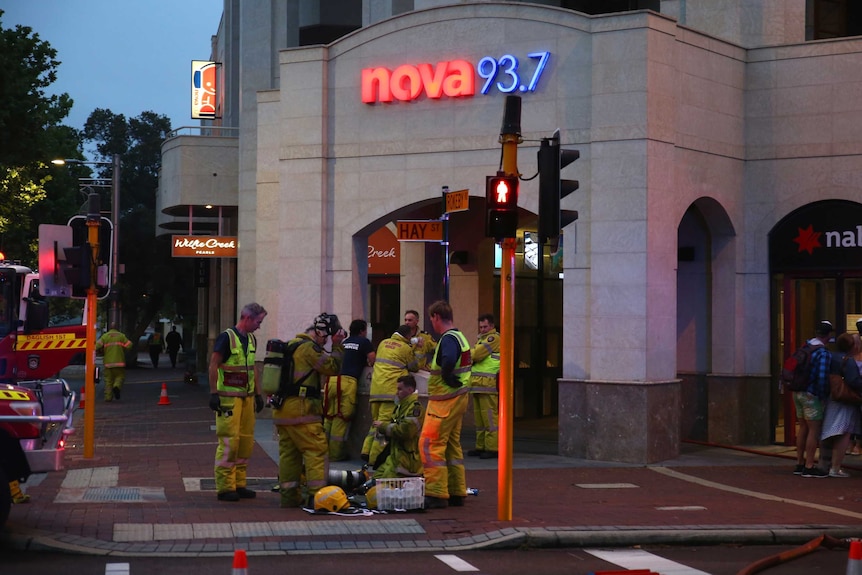 A group of fire fighters standing in front of a  building with Nova 93.7 neon sign