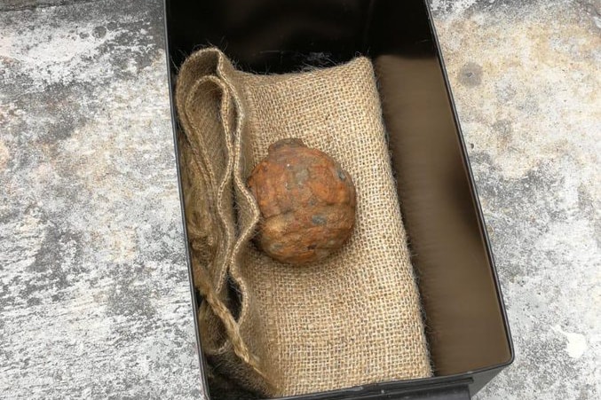 A rusted grenade sitting in a black box over burlap.