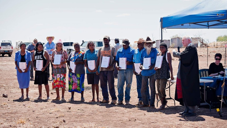 Federal Court Judge Richard White stands next to a group of Indigenous people holding native title certificates.