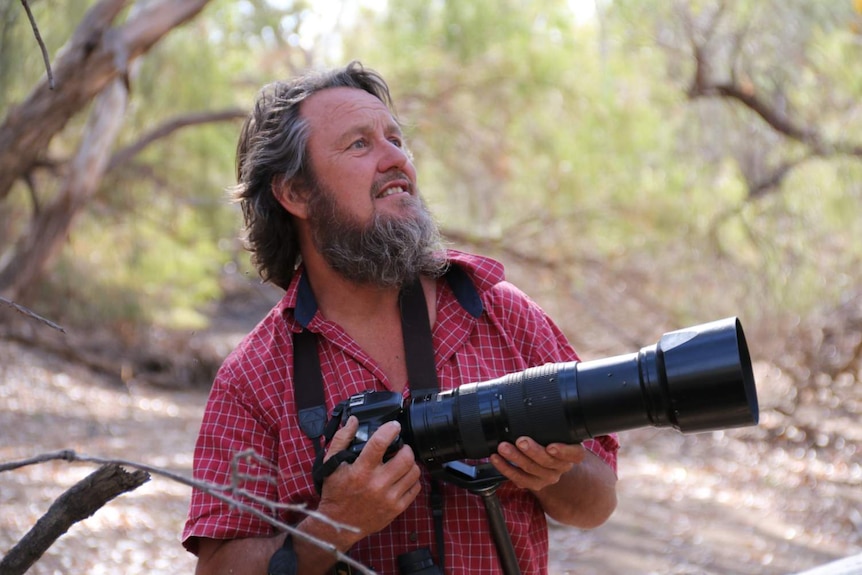 A man looks up at the sky holding a camera