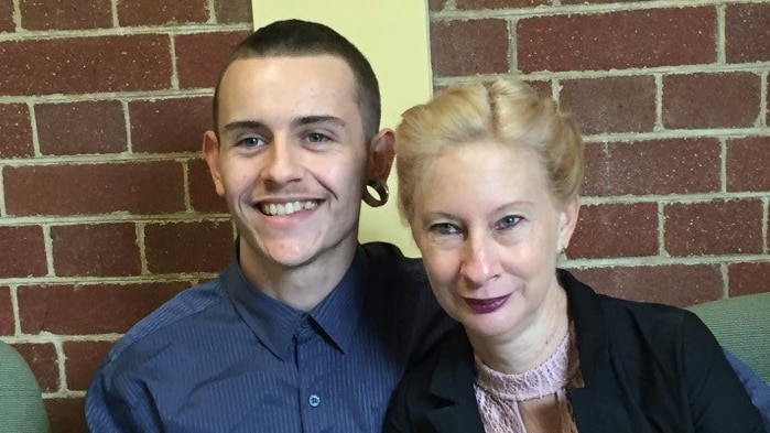 A woman sits next to a young man in front of a brick wall.