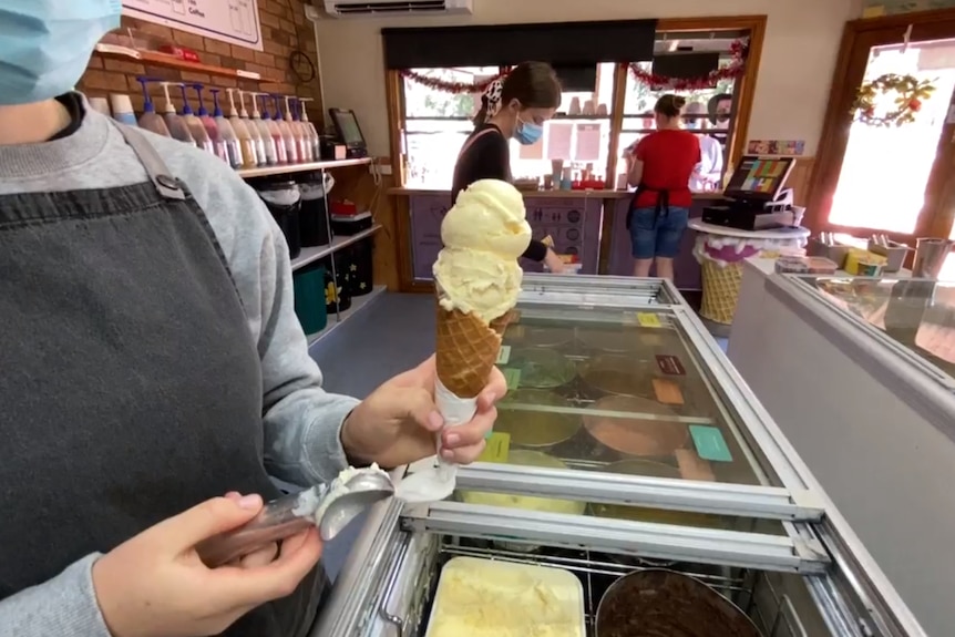 Three workers prepare and serve ice creams to customers in a corner shop.
