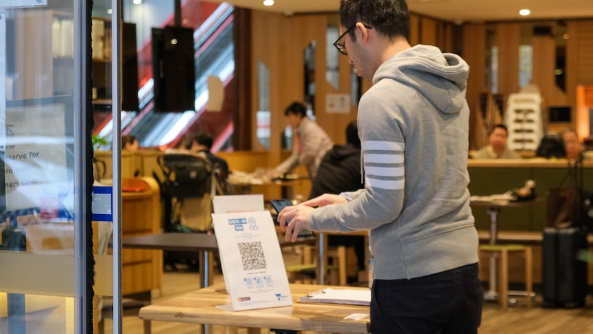 A man wearing a hoodie stands in front of a QR code with his phone.