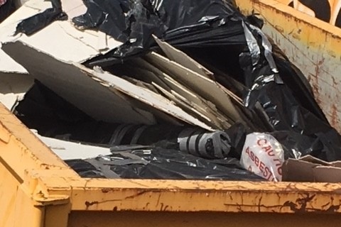 Black plastic bags and asbestos in a large yellow metal bin.