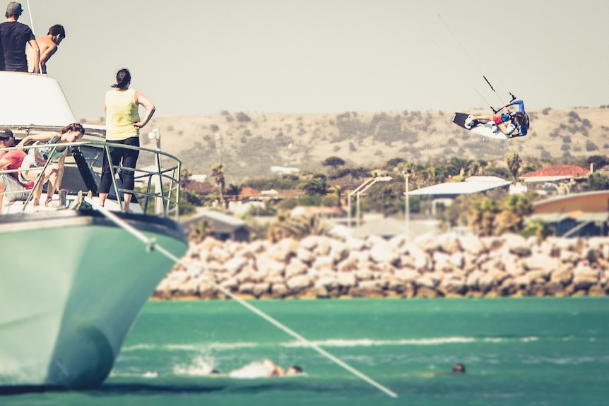 man in the air while kitesurfing, in ocean, boat to the left side of frame with people