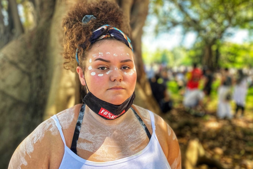 a teenager looking into the camera, her hair is done up and her mask is hanging beneath her chin