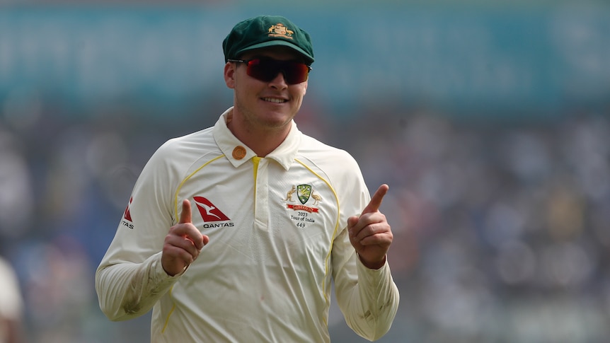 An Australian cricketer wearing his baggy green cap, signals on the field with his fingers.