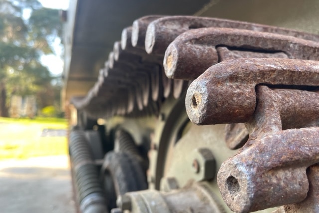 Rusty cylinders of metal attached to a khaki cog system on the bottom of a military vehicle.