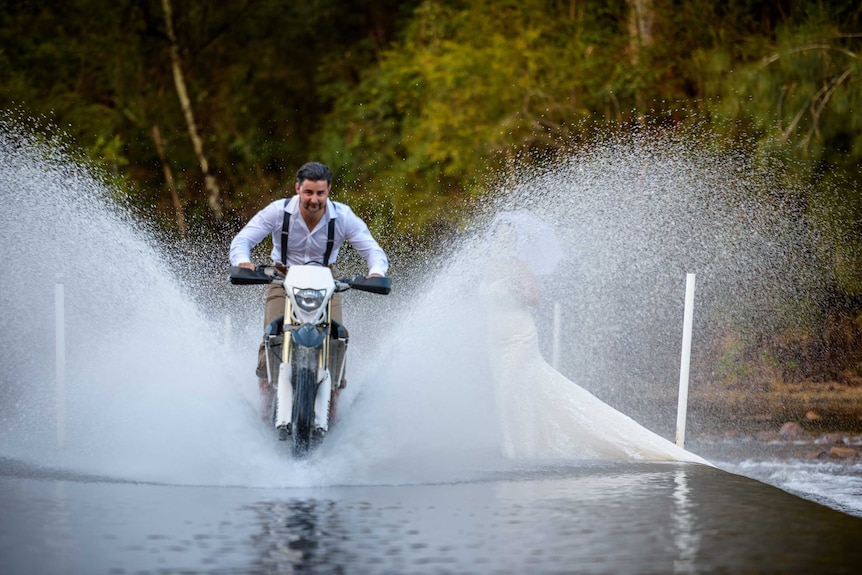 A man on a motorcycle speeds across a creek crossing, spraying up water.