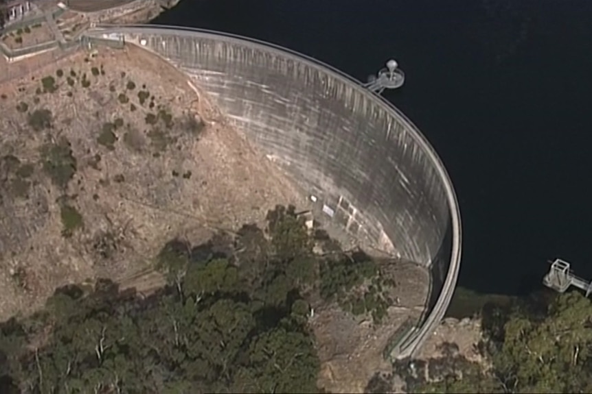 A round dam wall with water on the right and bushland on the left