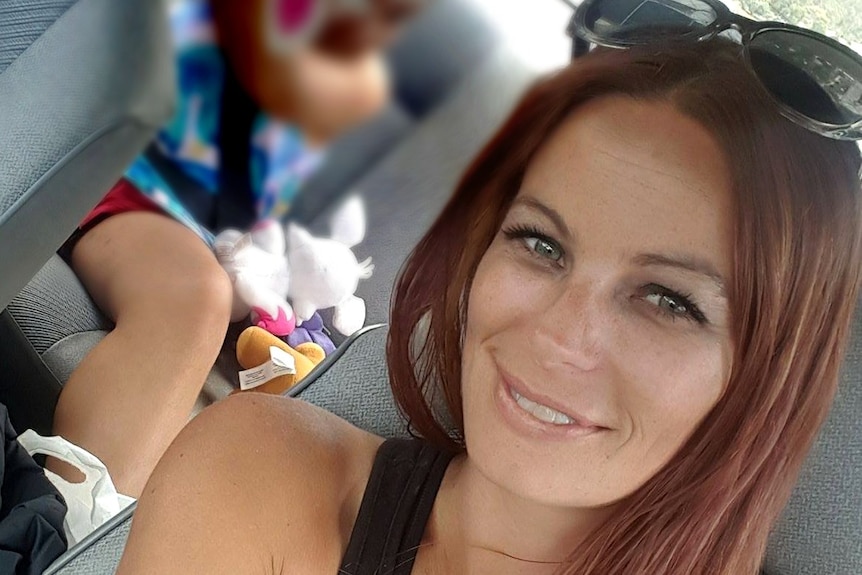 Jacqui Purton, a smiling woman in her 30s with long reddish-brown hair, takes a selfie in a car.