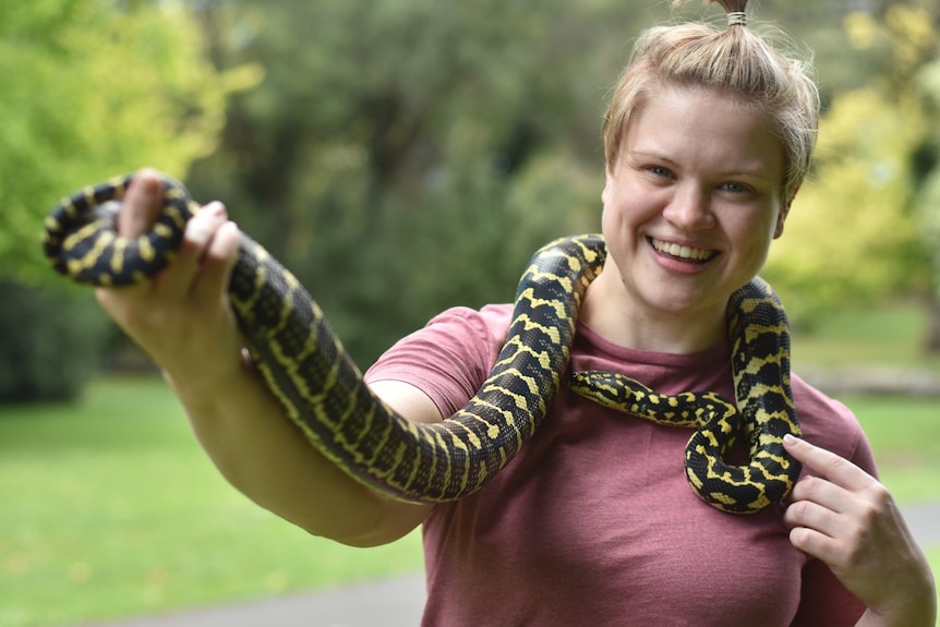 Woman holds snake around her shoulders.