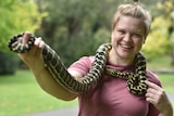 Woman holds snake around her shoulders.