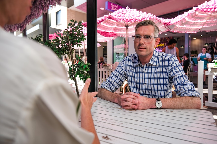 a man wearing glasses sitting at a cafe table being interviewed by a woman