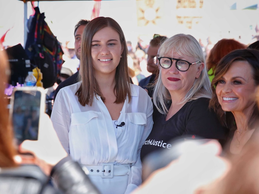 A young woman with brown hair wearing white standing next to an older woman with grey hair, smiling for a photo