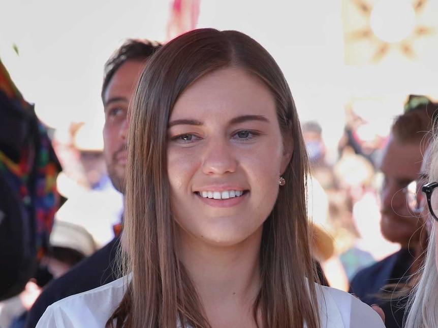 A young woman with brown hair wearing white standing next to an older woman with grey hair, smiling for a photo