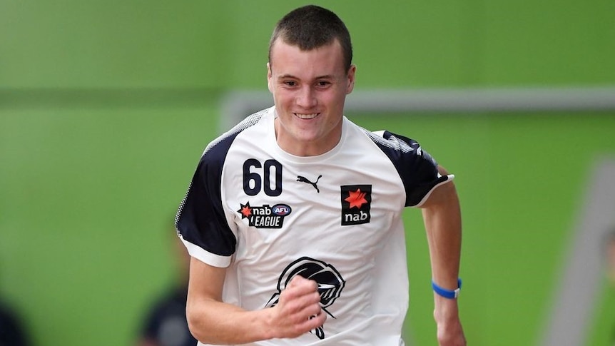 An Australian rules footballer runs down a track with a smile on his face.