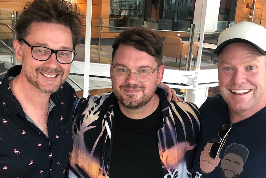 Steven Gates, Tim Shiel and Peter Helliar smile and pose arm in arm in the Double J studios