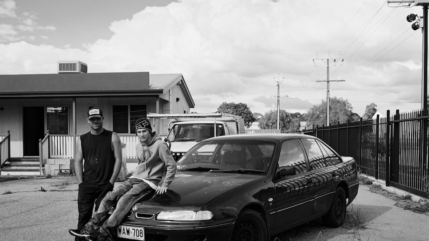 Two young men stand near a Holden car in an unused car yard in Elizabeth, South Australia.