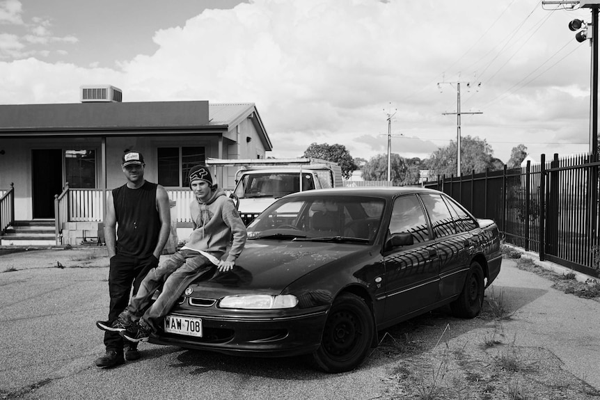 Two young men stand near a Holden car in an unused car yard in Elizabeth, South Australia.